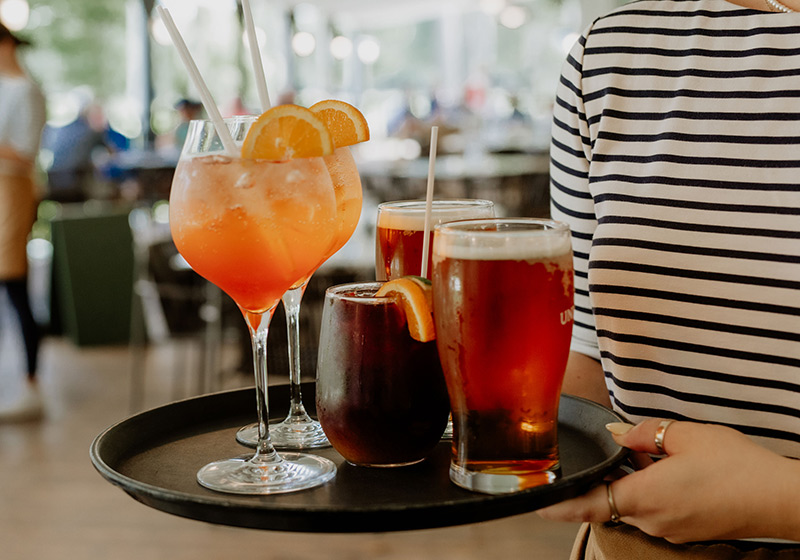 Une serveur avec un plateu de cocktails et bières